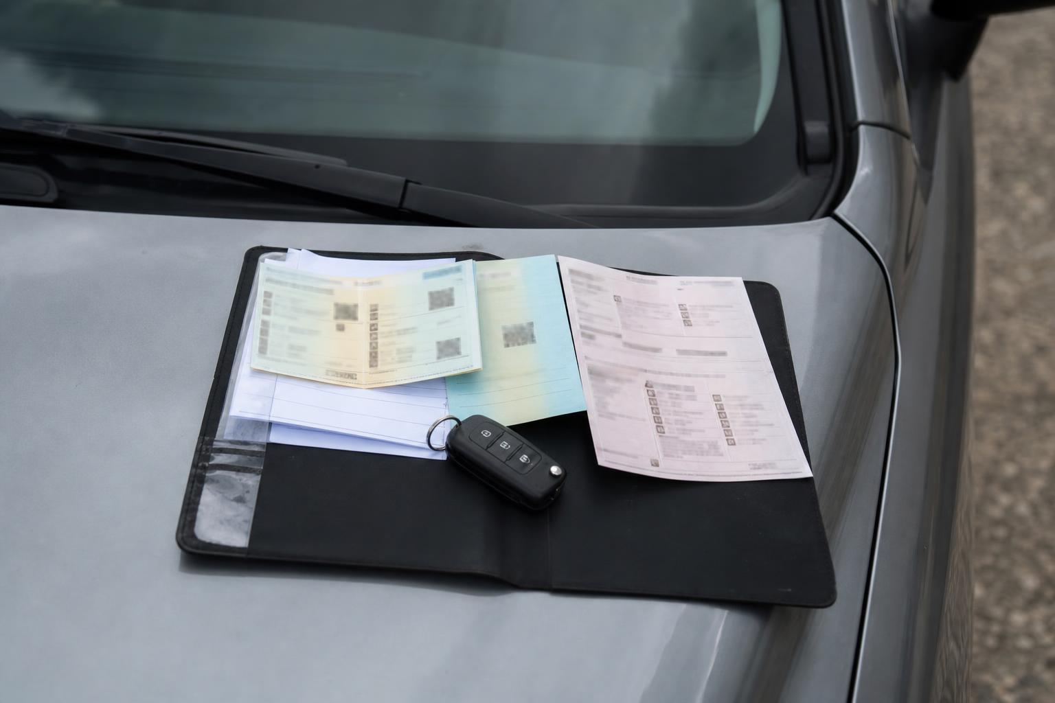 Használt autó motorháztetején elhelyezett járműokmányok és autókulcs, a törzskönyv ellenőrzését szemléltetve
