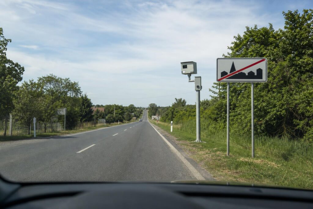 Autó közeledik a lakott terület végét jelző táblához, előtte traffipax látható az út mellett
