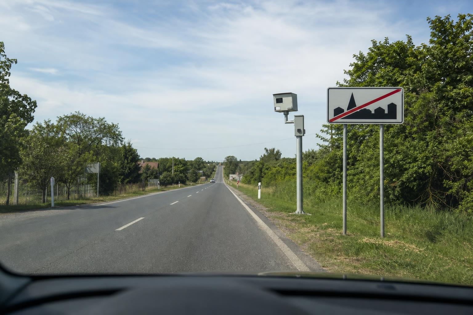 Autó közeledik a lakott terület végét jelző táblához, előtte traffipax látható az út mellett