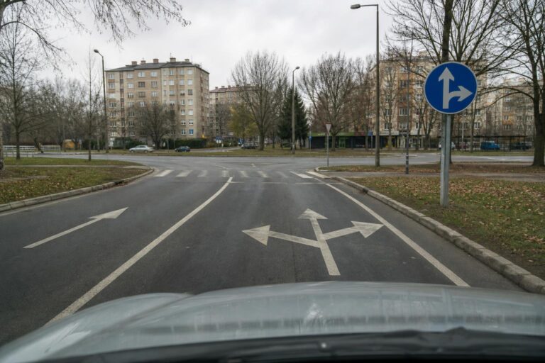 Közúti jelzőtábla és eltérő irányt mutató útburkolati nyilak egy útkereszteződésben