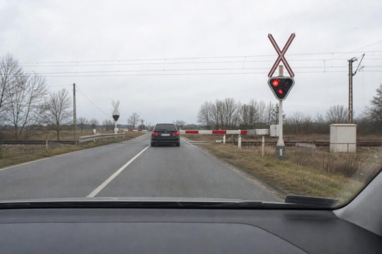 Autó közeledik egy vasúti átjáróhoz piros fényjelzés és leeresztett sorompó előtt