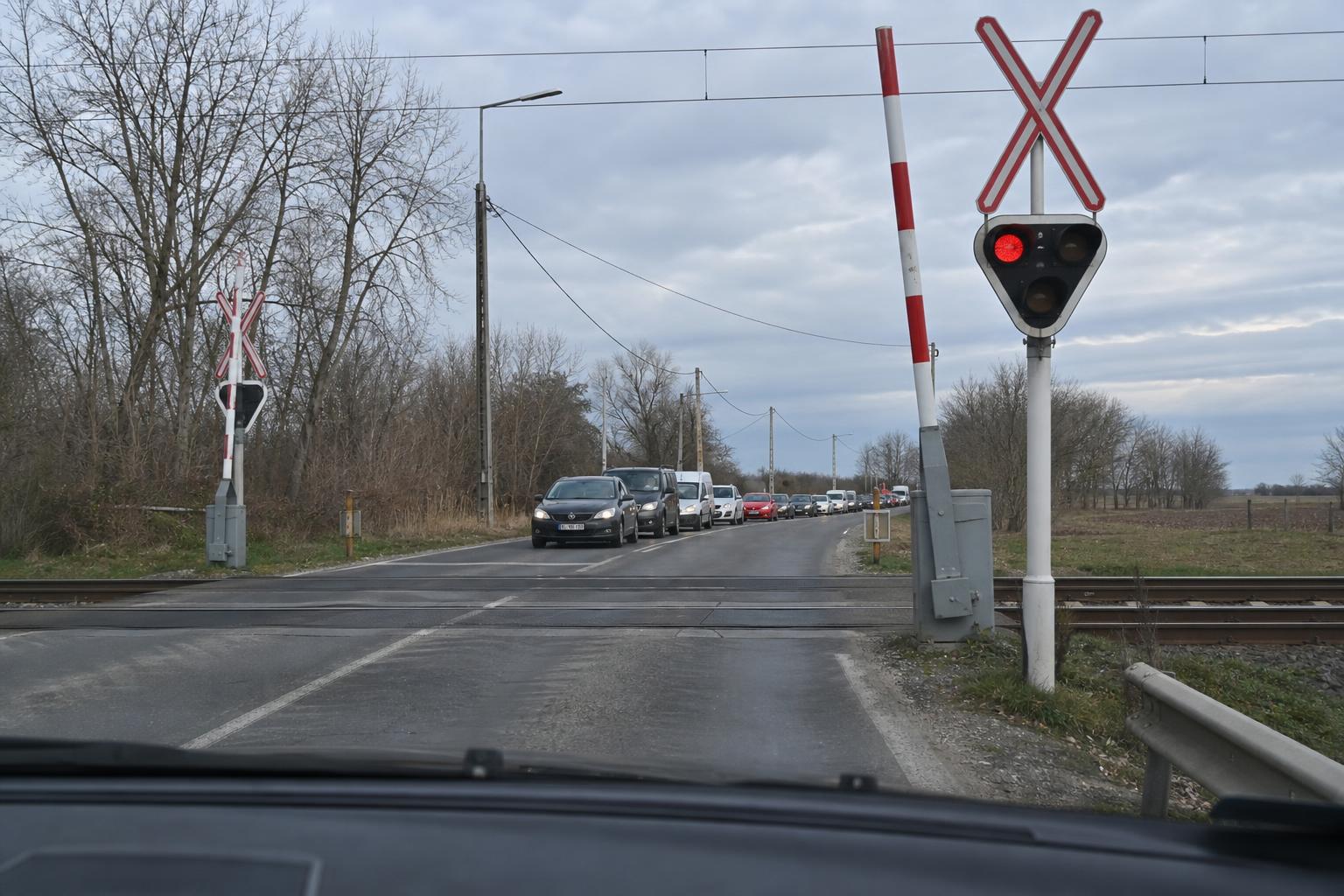 Autó áll a vasúti átjáró előtt, miközben a túloldalon torlódik a forgalom