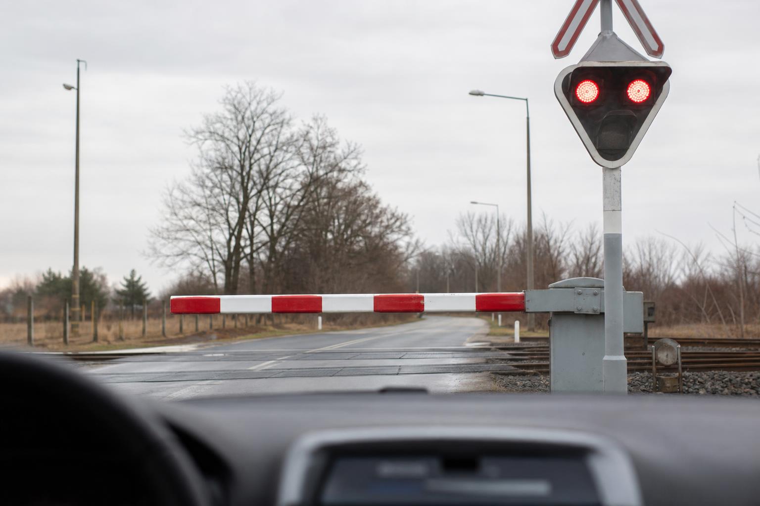 Autó közeledik villogó piros jelzésű, leengedett félsorompós vasúti átjáróhoz