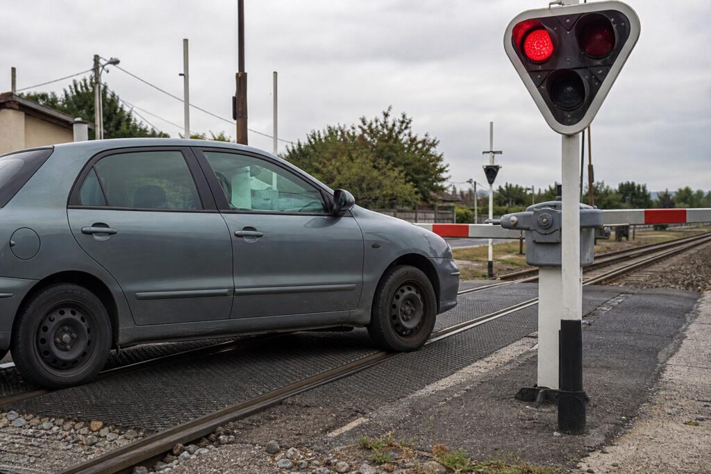 Elakadt személyautó vasúti átjáróban leeresztett sorompó és villogó jelzőfény mellett