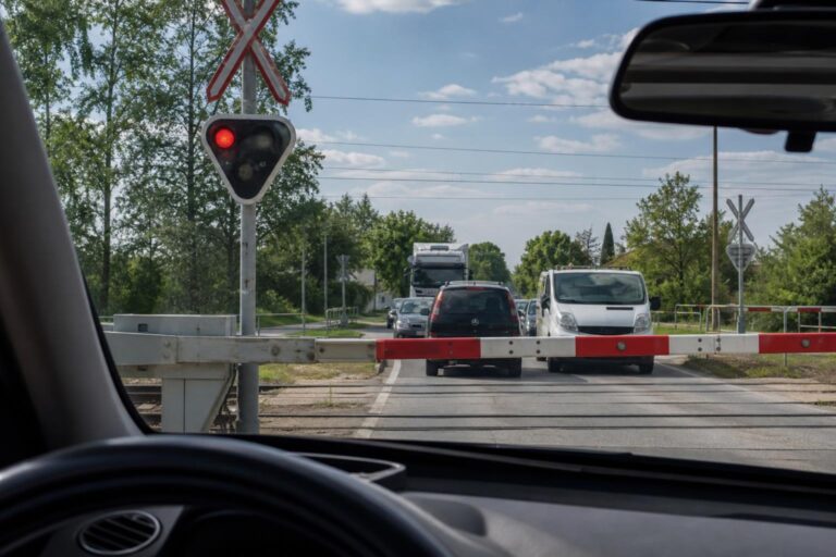 Autó várakozik a vasúti átjáró előtt leeresztett sorompónál, a sínekre behajtás nélkül
