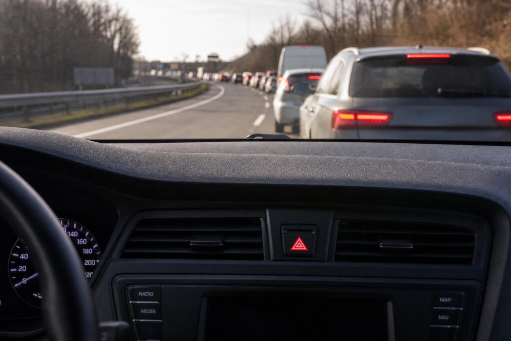 Autó műszerfala vészvillogó-jelzéssel, előtte hirtelen kialakult torlódás és fékező járművek egy autópályán
