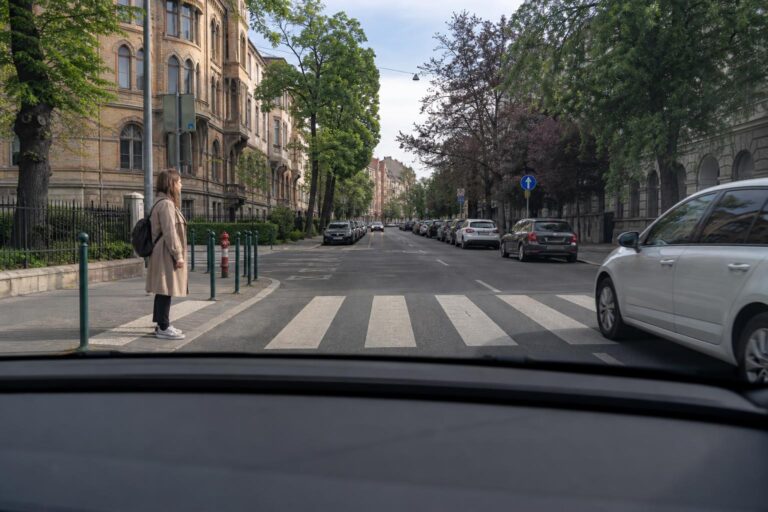 Autó közelít a zebrához, miközben egy gyalogos átkelésre készül a járdaszegélynél