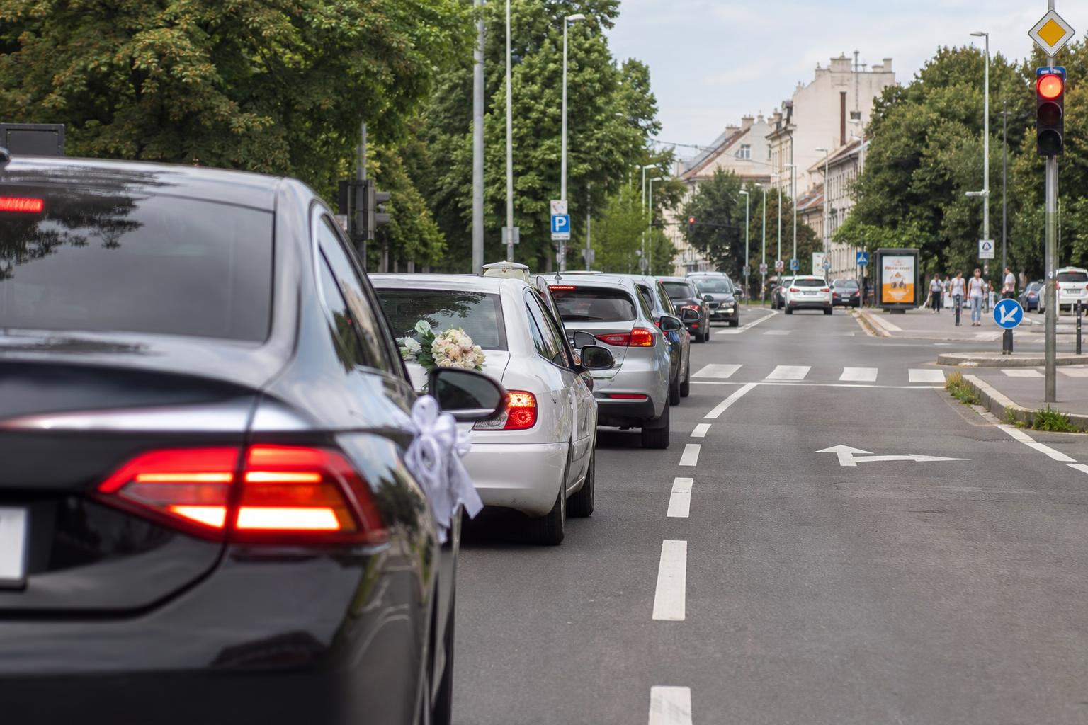 Esküvői konvoj szabályosan haladó autókkal városi úton, látható jelzőlámpával és útburkolati jelekkel