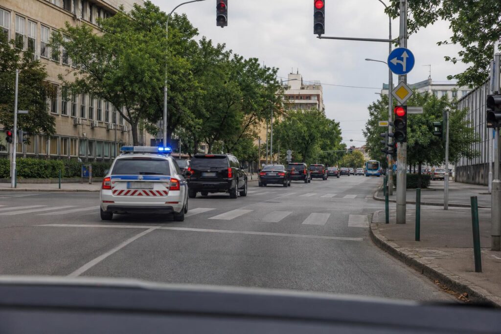 Rendőri felvezetés alatt haladó zárt konvoj rendőrautóval egy városi kereszteződésben