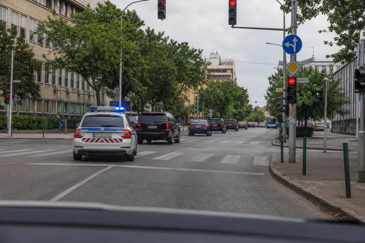 Rendőri felvezetés alatt haladó zárt konvoj rendőrautóval egy városi kereszteződésben